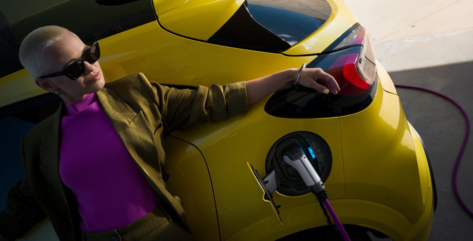 A woman leaning against a yellow electric Ford Capri that is connected to an EV charger.