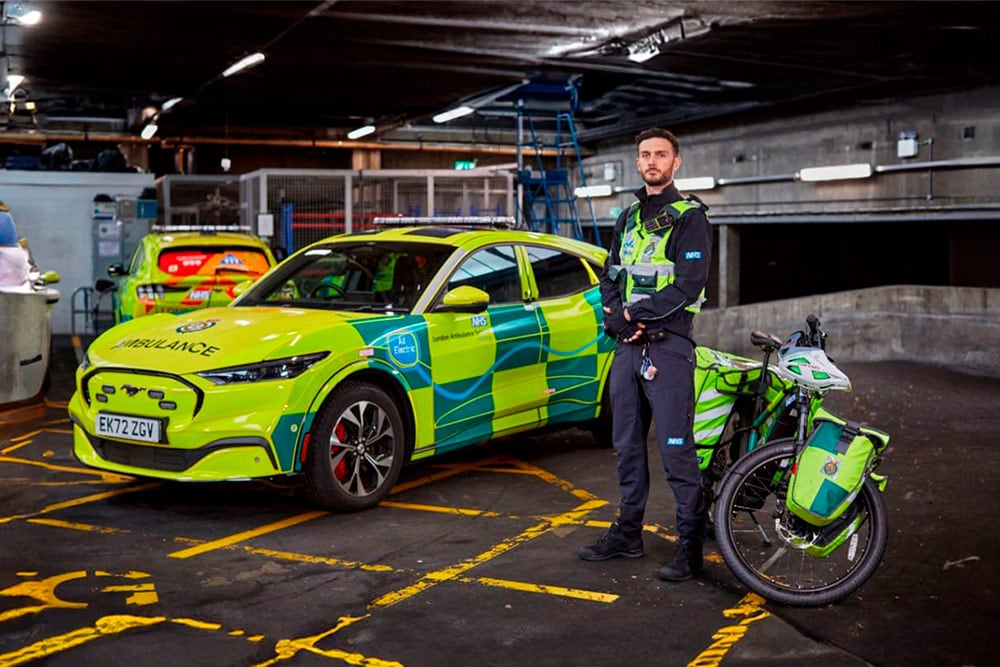 A London Ambulance Service paramedic standing next to a Ford Mustang Mach-E rapid response vehicle.