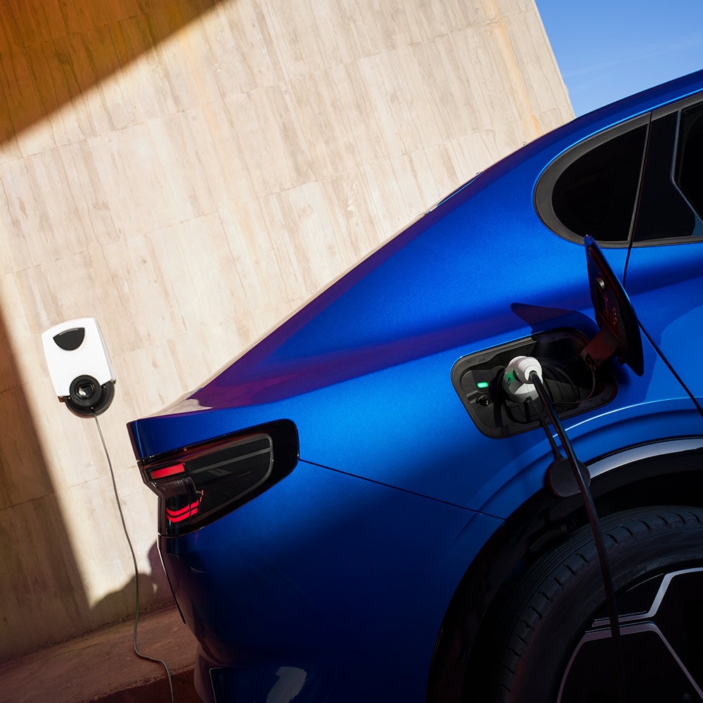 A rear view of a blue Ford Capri eletric vehicle plugged in to an EV home charging point.