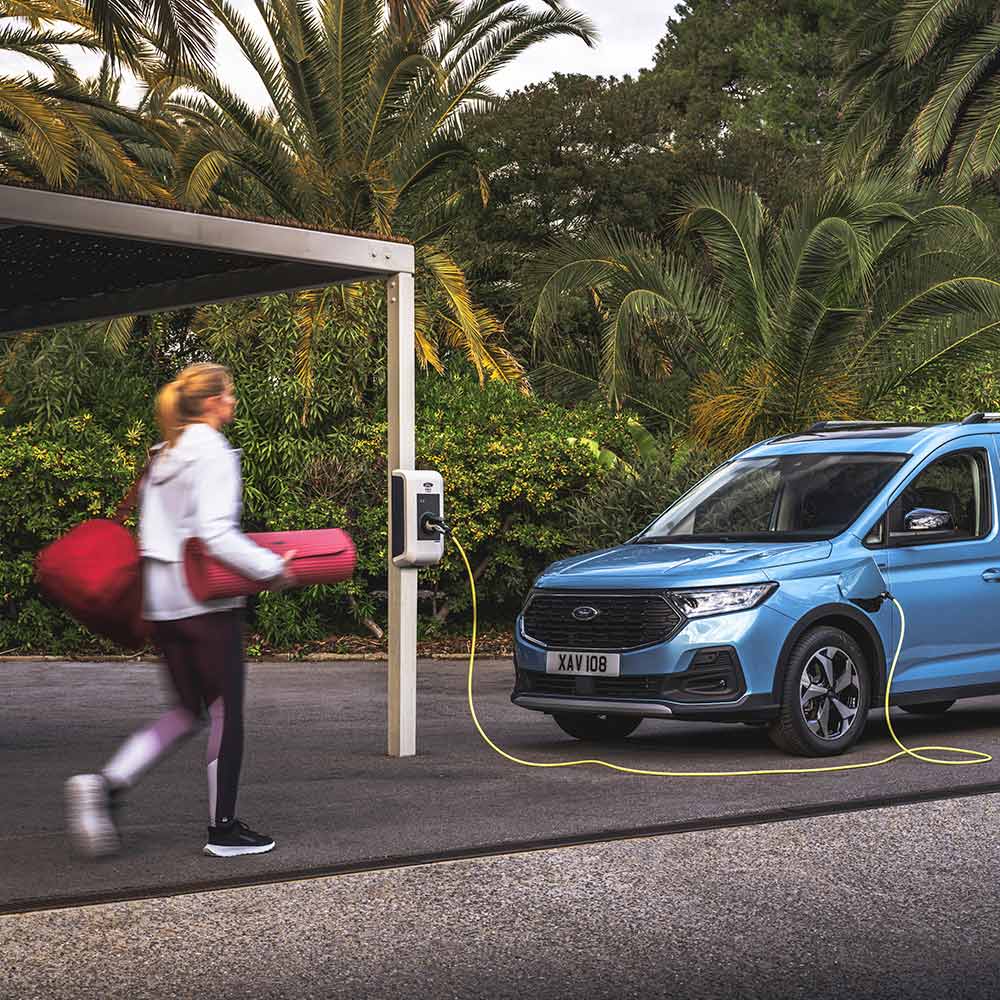 A person with a yoga mat walking towards a Ford Tourneo Connect plug-in hybrid van.