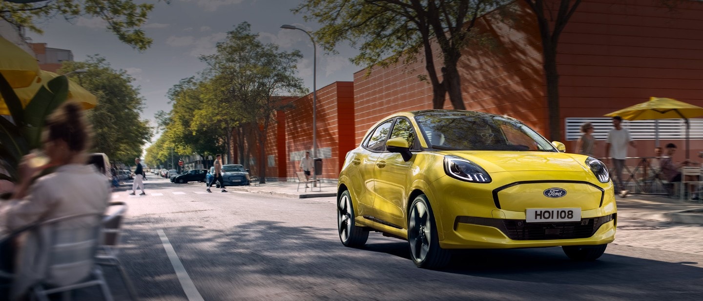 Front view of a yellow electric Ford Puma Gen-E® driving along a city road.