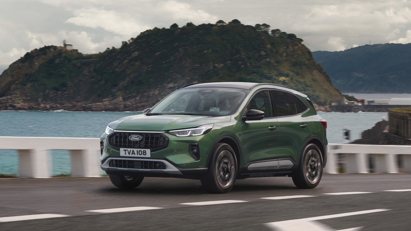 A green Ford Kuga drives along a coastal road, with a cliff and sea in the background